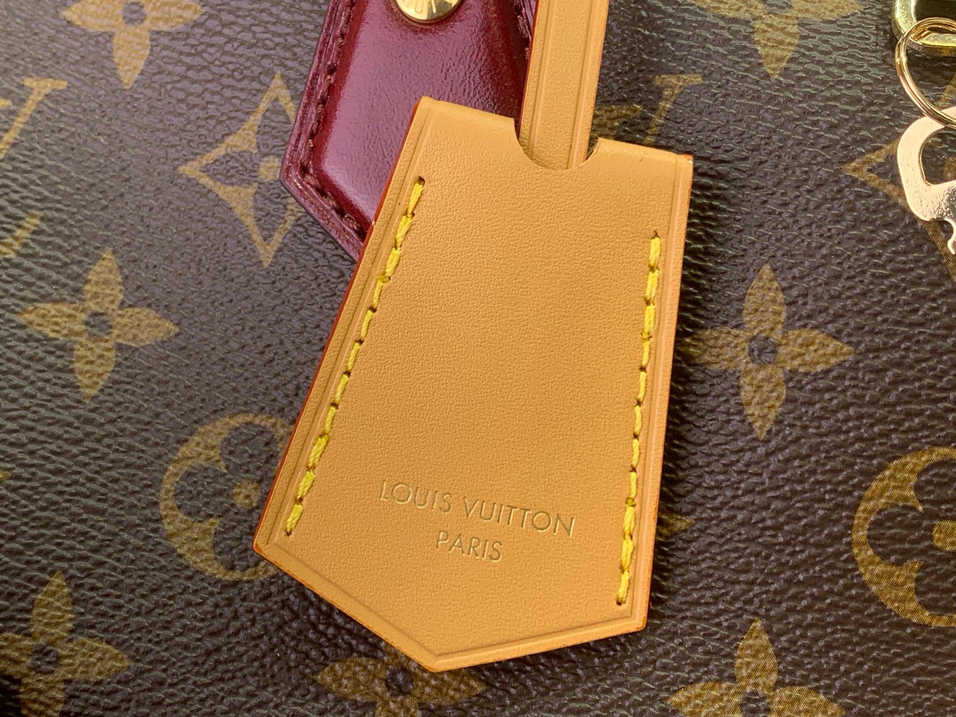 Yellow luggage tag with Louis Vuitton text on monogram bag handle
