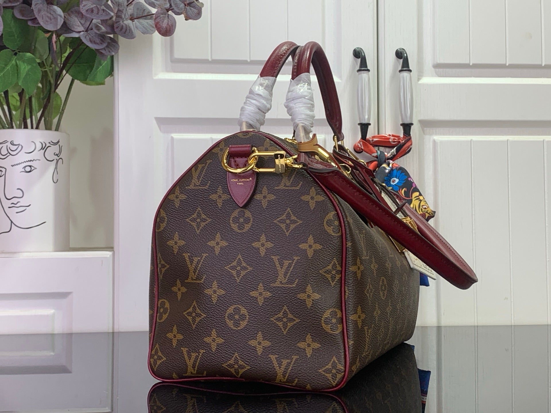 Monogram tote bag with burgundy handle, side view, and gold hardware