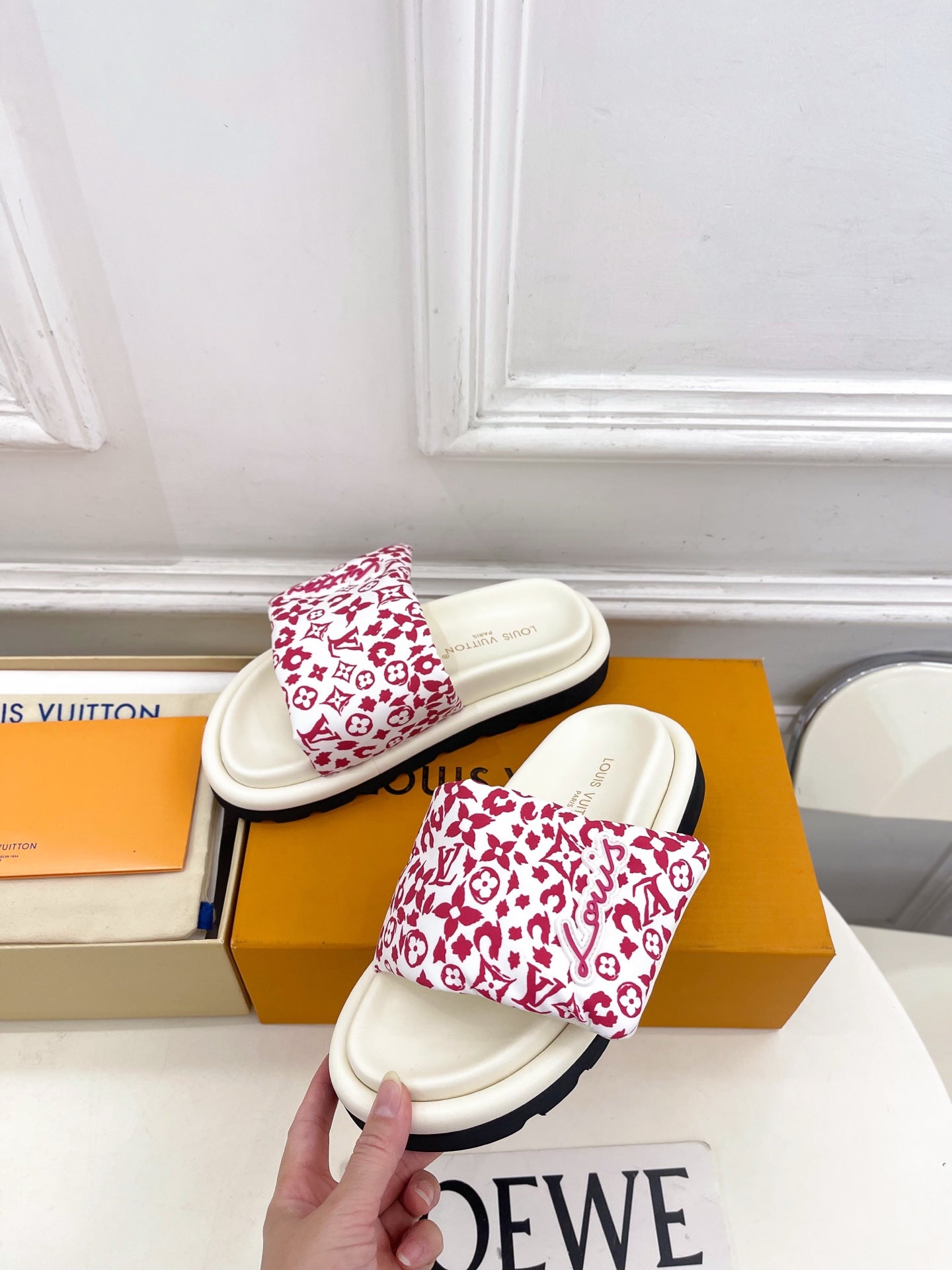 Louis Vuitton slide sandal held in hand; white strap with red monogram print