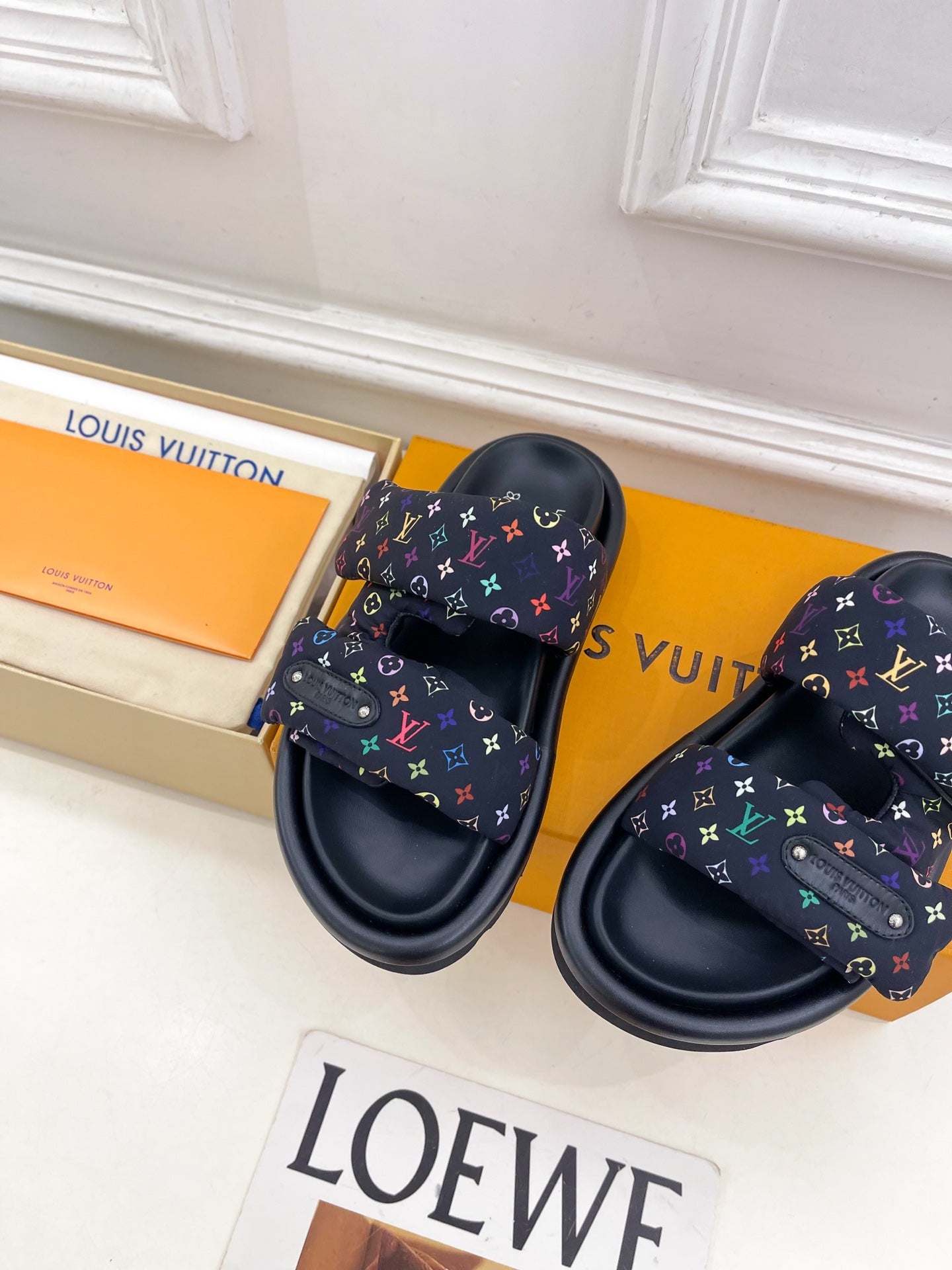 Luxury slide sandals on display; dark navy monogram straps with multicolor pattern