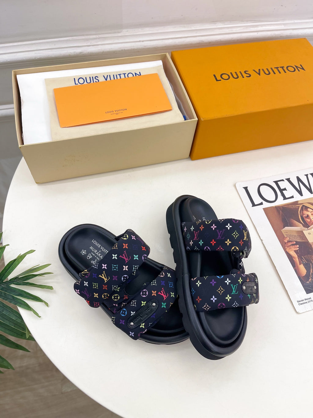 Pair of luxury slide sandals on box; dark navy monogram straps with multicolor print