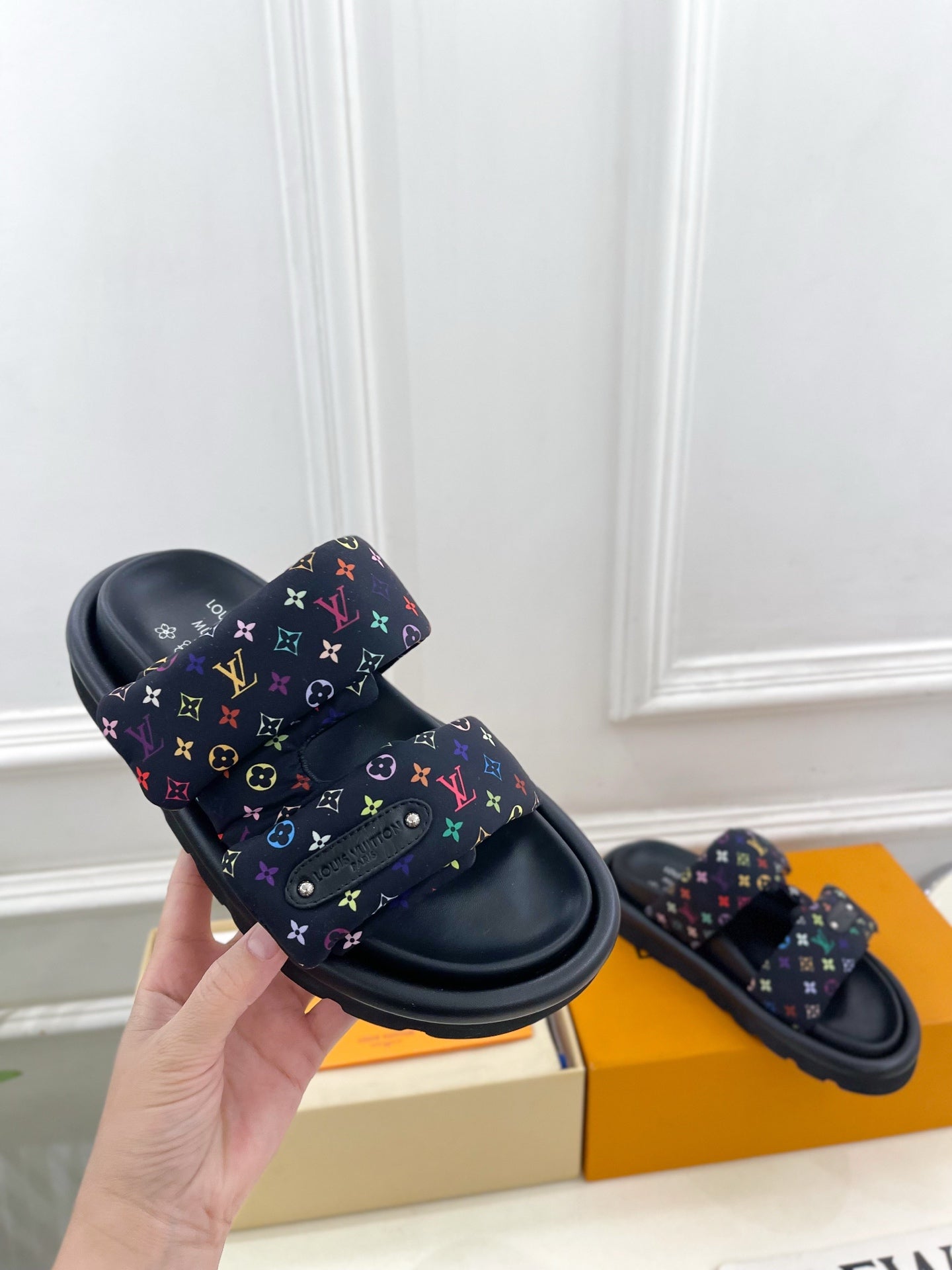 Luxury slide sandals, one shoe held up; dark navy monogram strap with multicolor accents