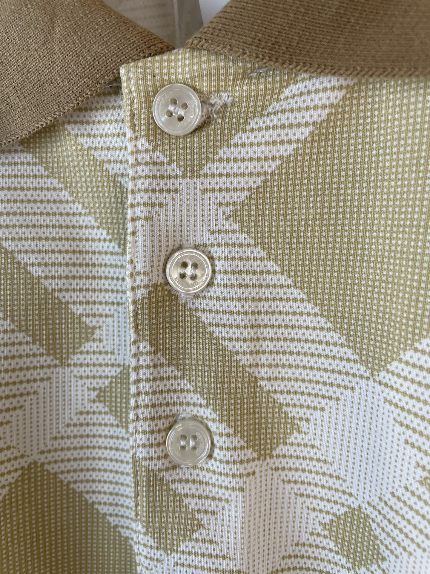 Polo shirt button placket with three white buttons on yellow-and-white check fabric