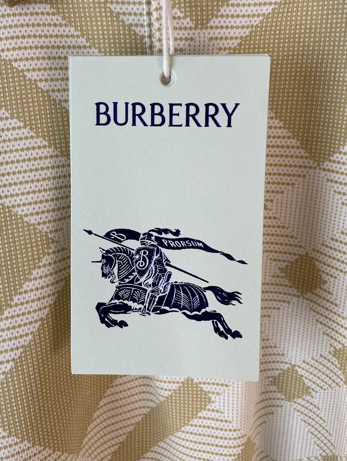 Burberry clothing hang tag with knight logo over yellow-and-white check fabric