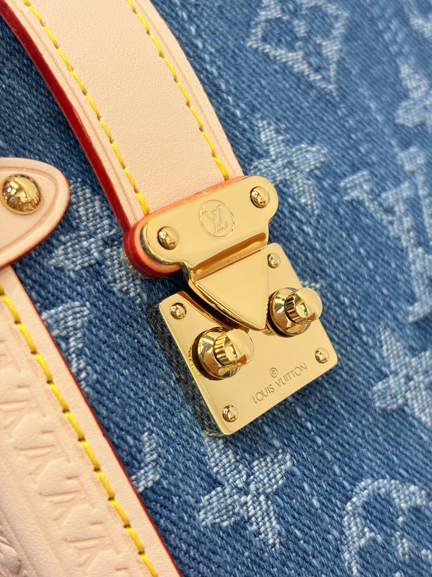 Louis Vuitton bag close-up of gold clasp and white leather tabs on blue canvas