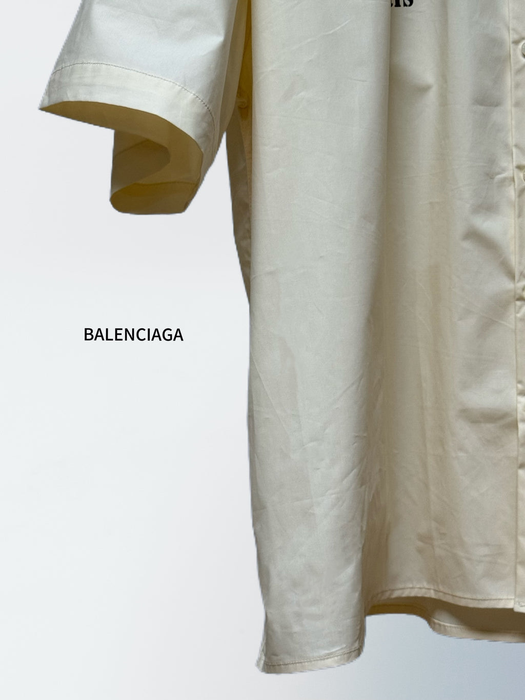 Balenciaga cream short-sleeve shirt, curved hem with button front and partially visible sleeve cuff.