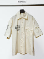 Balenciaga cream short-sleeve button shirt with pointed collar and chest pockets, logo print.