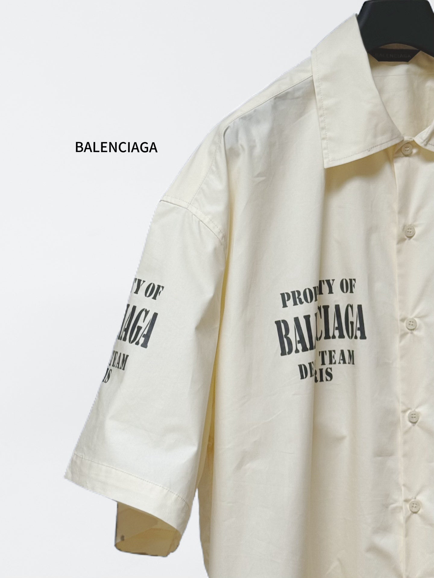 Cream short-sleeve button-up shirt with front pocket and sleeve logo text