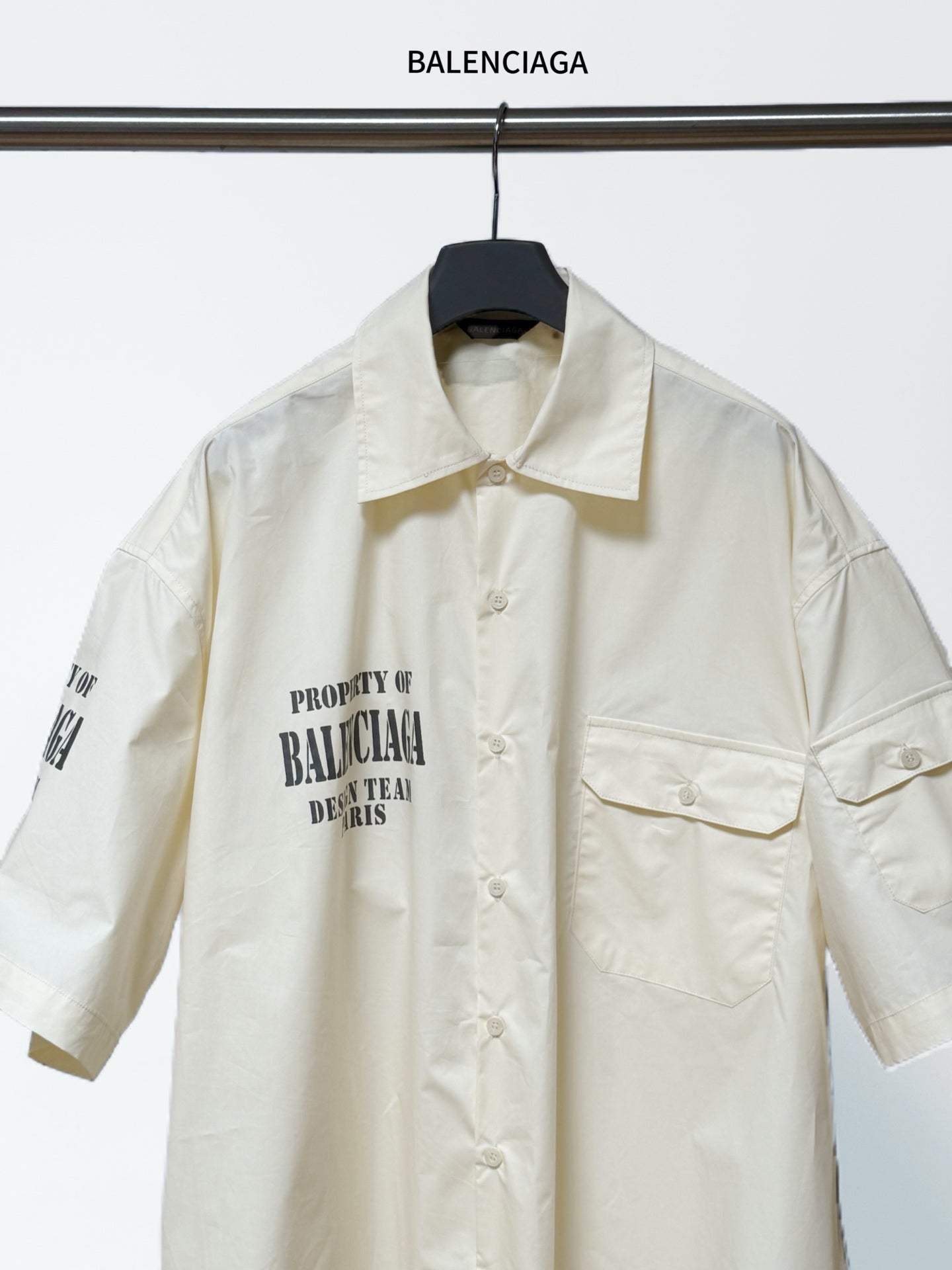 Balenciaga cream short-sleeve button shirt with pointed collar, chest pockets, and front text.