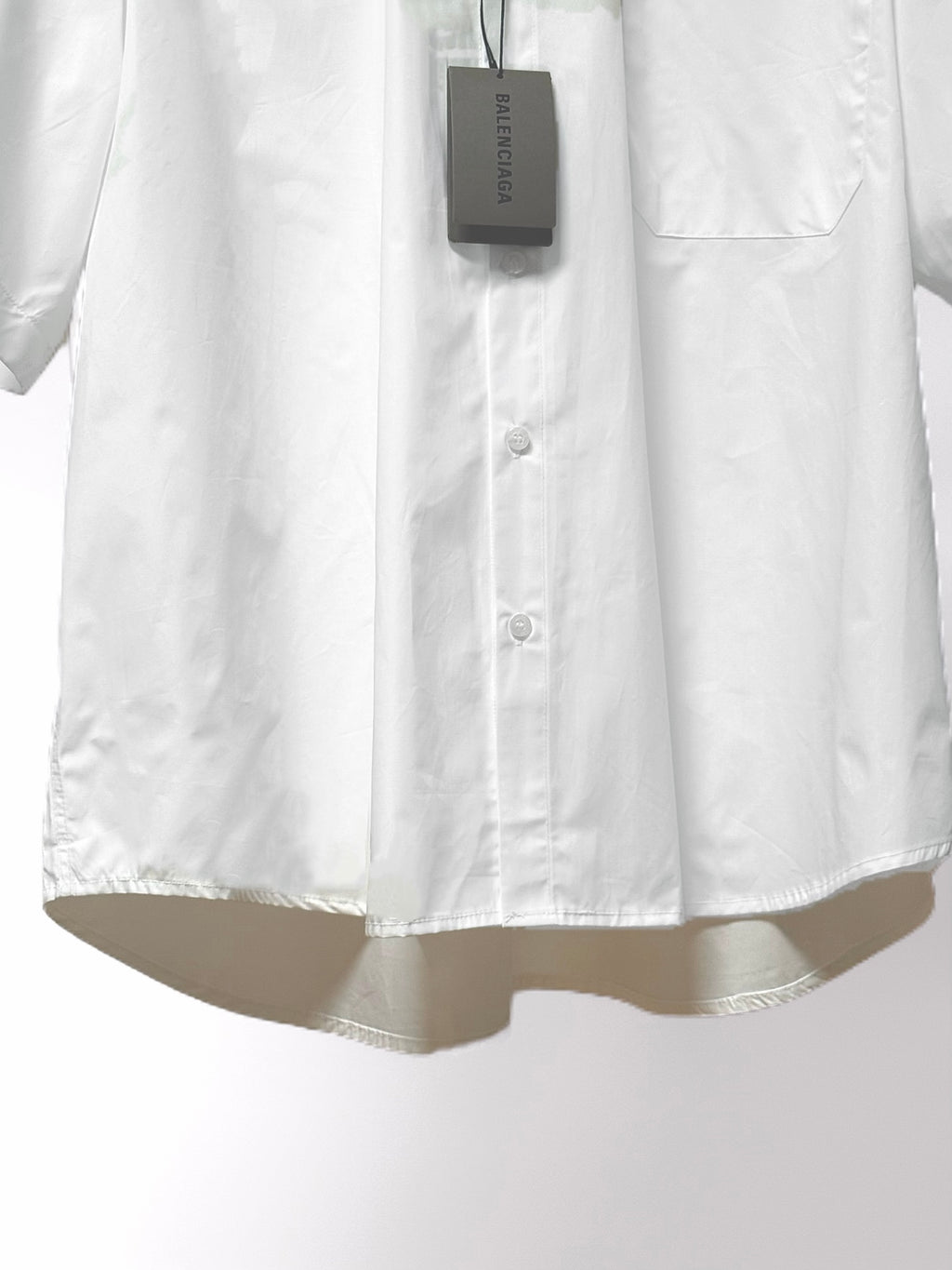 Balenciaga white short-sleeve shirt button placket and hanging tag near hem