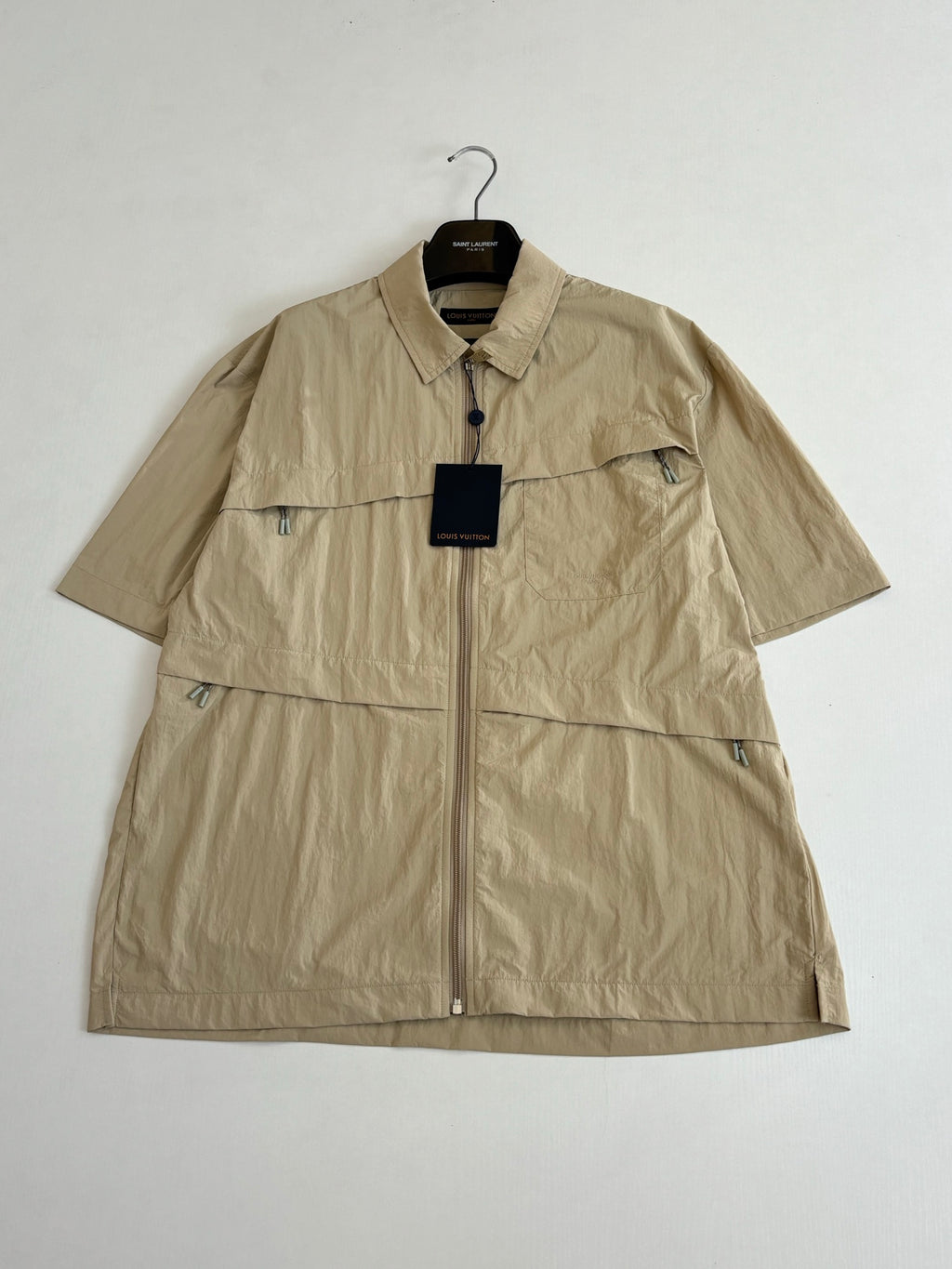 Beige short-sleeve zip jacket with pointed collar and visible logo hangtag