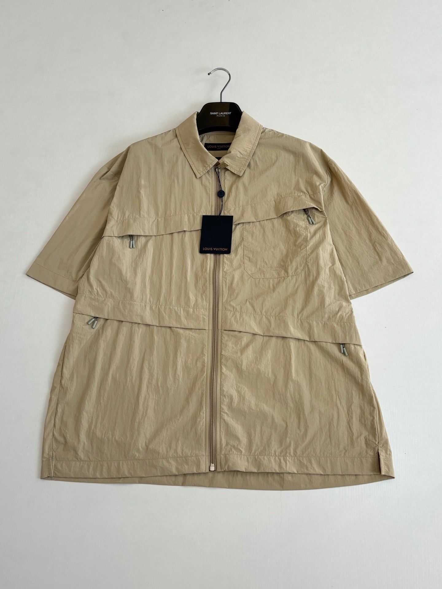 Beige short-sleeve zip jacket with pointed collar and visible logo hangtag