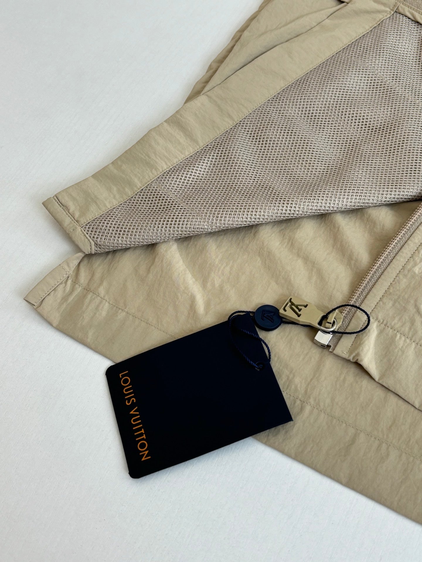 Beige Louis Vuitton jacket with mesh-lined pocket opening and navy hangtags