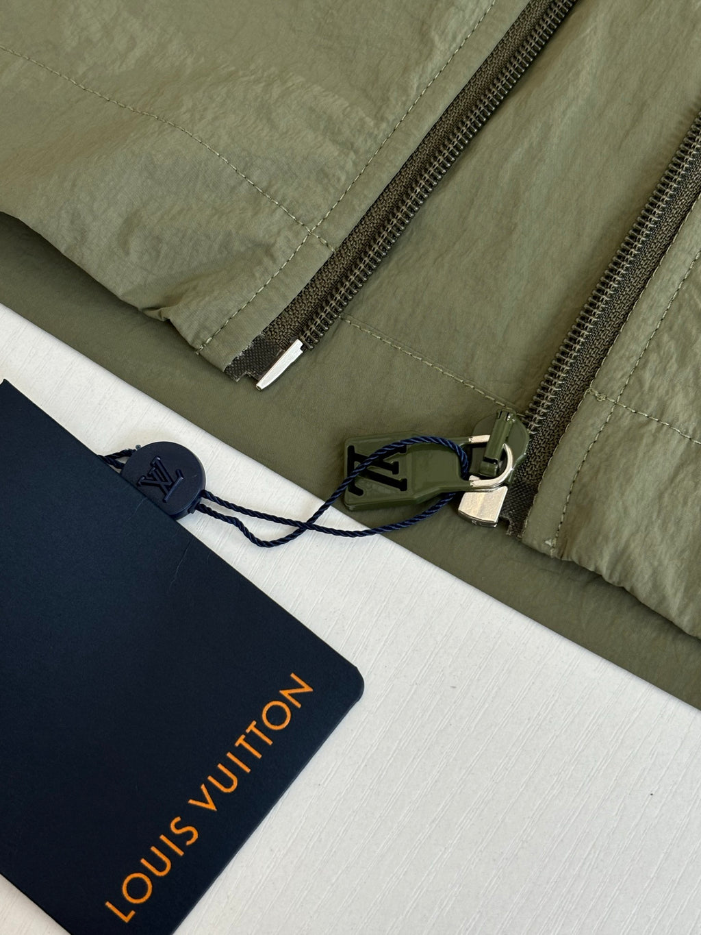 Olive green jacket zipper with inner mesh panel and hanging brand tags.
