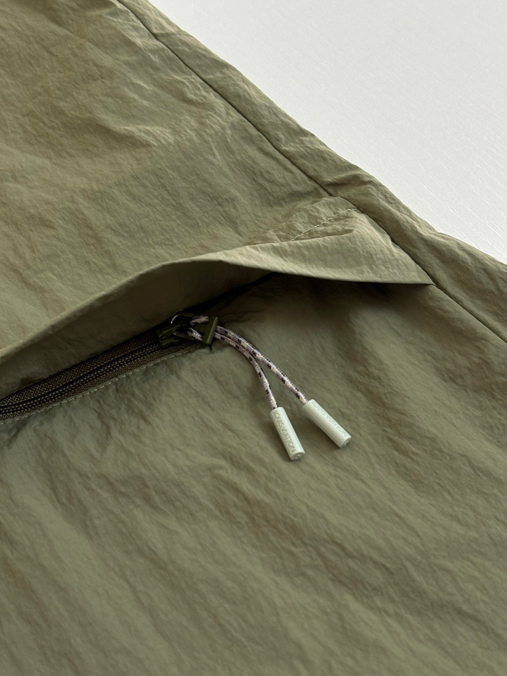Olive green jacket sleeve cuff with zipper pull and drawstring detail.