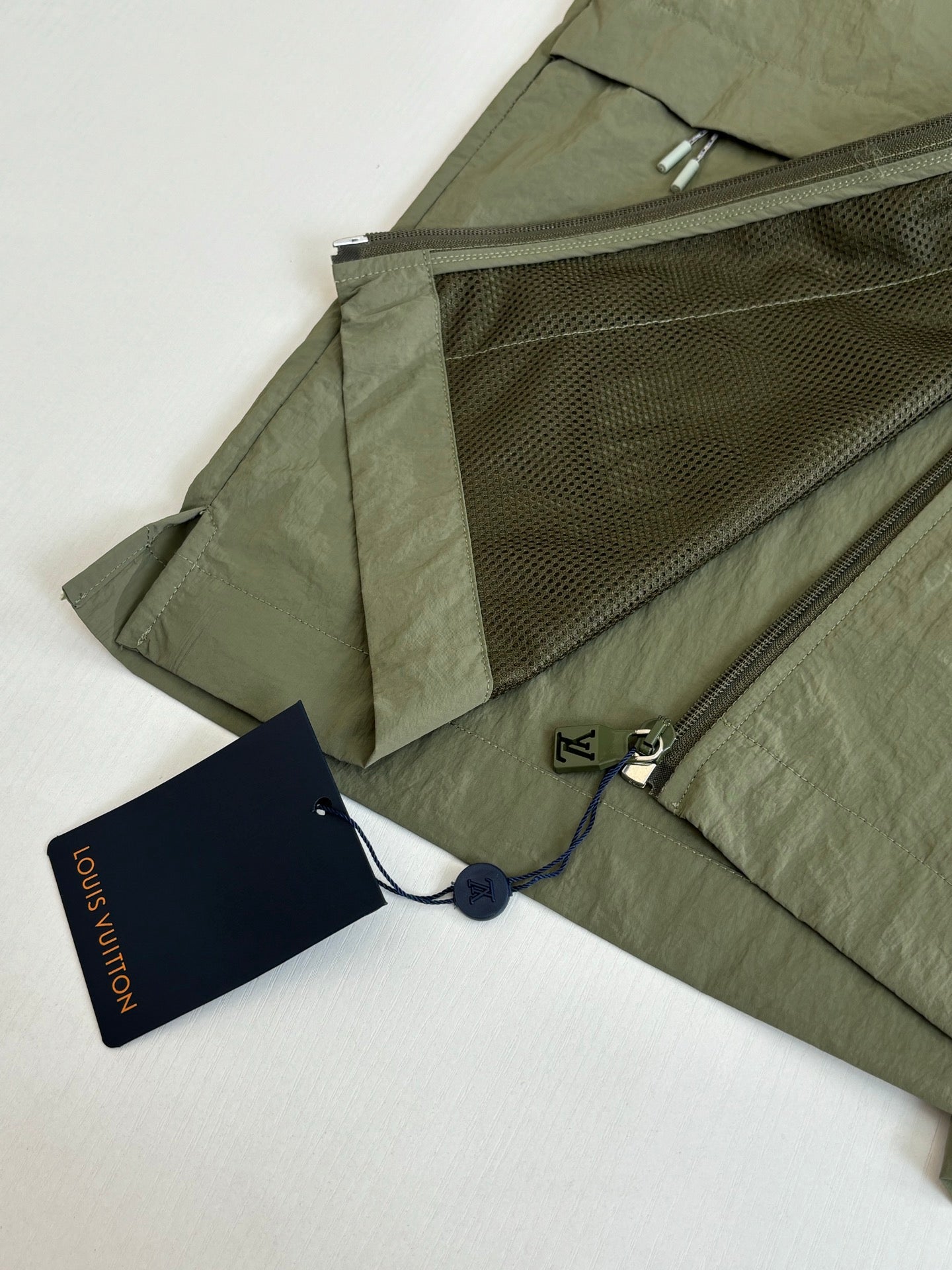 Olive green jacket with interior mesh pocket, zipper, and blue hang tags.