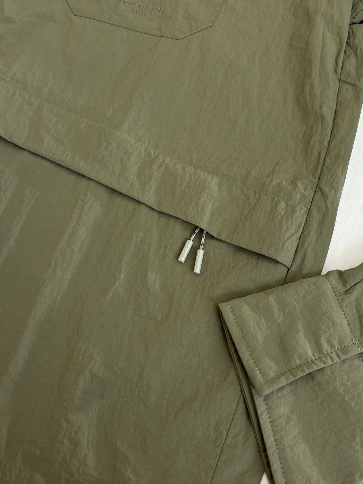 Olive green jacket back hem with zipper and layered fabric trim.