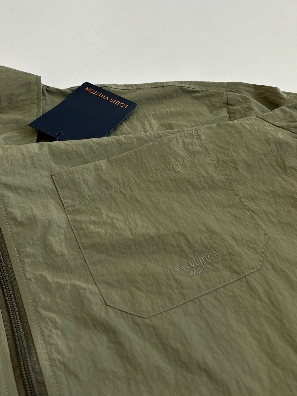 Olive green jacket front with zipper and interior pocket label tags.