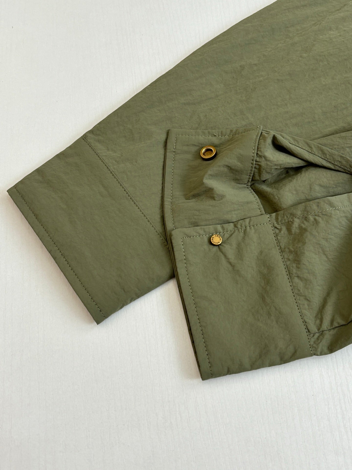 Olive jacket with flap pockets and brass snap buttons on cuff