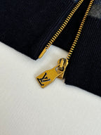 Gold-tone zipper pull and bar on black ribbed cuff of check knit sweater