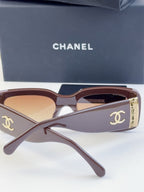 Pair of square sunglasses with brown frames and tinted lenses, gold logo side detail