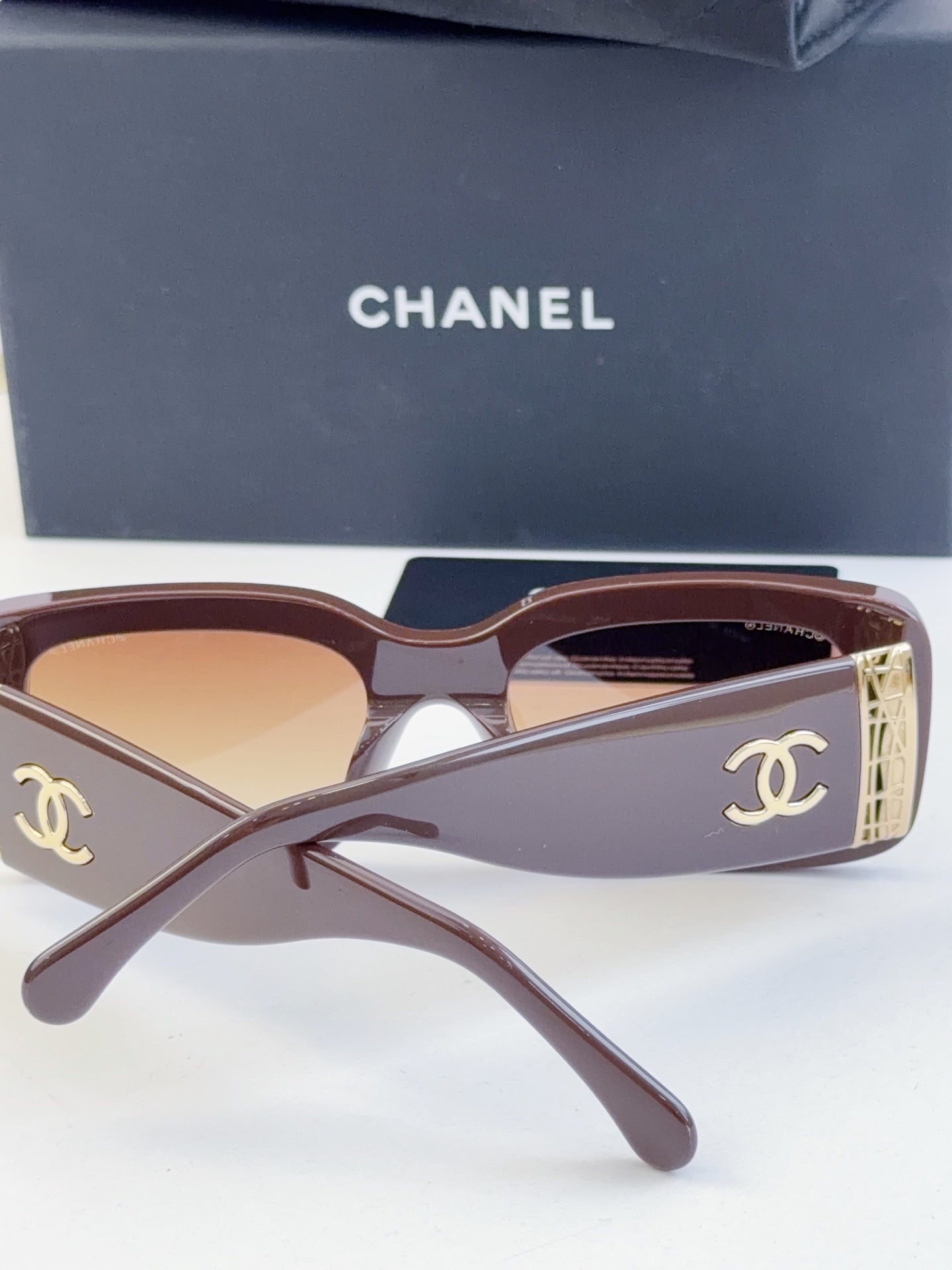 Pair of square sunglasses with brown frames and tinted lenses, gold logo side detail