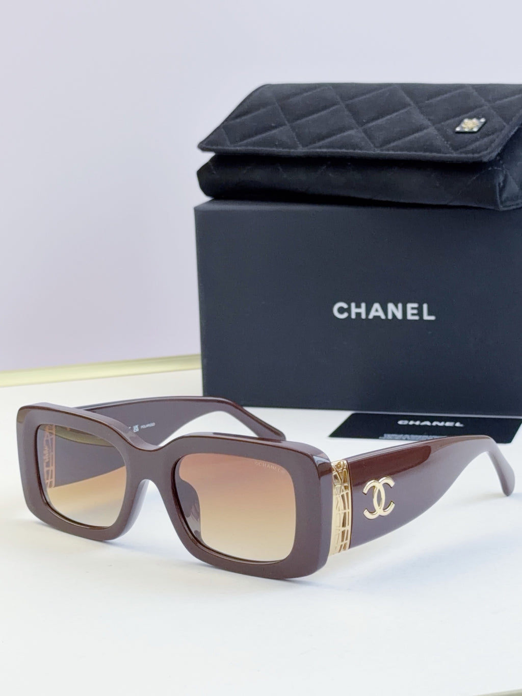 Square sunglasses with brown frames and tinted lenses, gold side logo detail