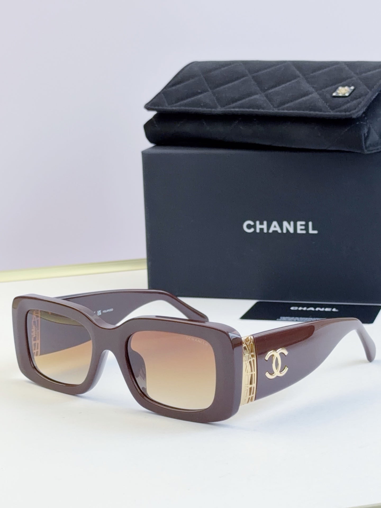 Square sunglasses with brown frames and tinted lenses, gold side logo detail