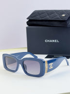 Square sunglasses with blue frames and tinted lenses, gold side logo detail
