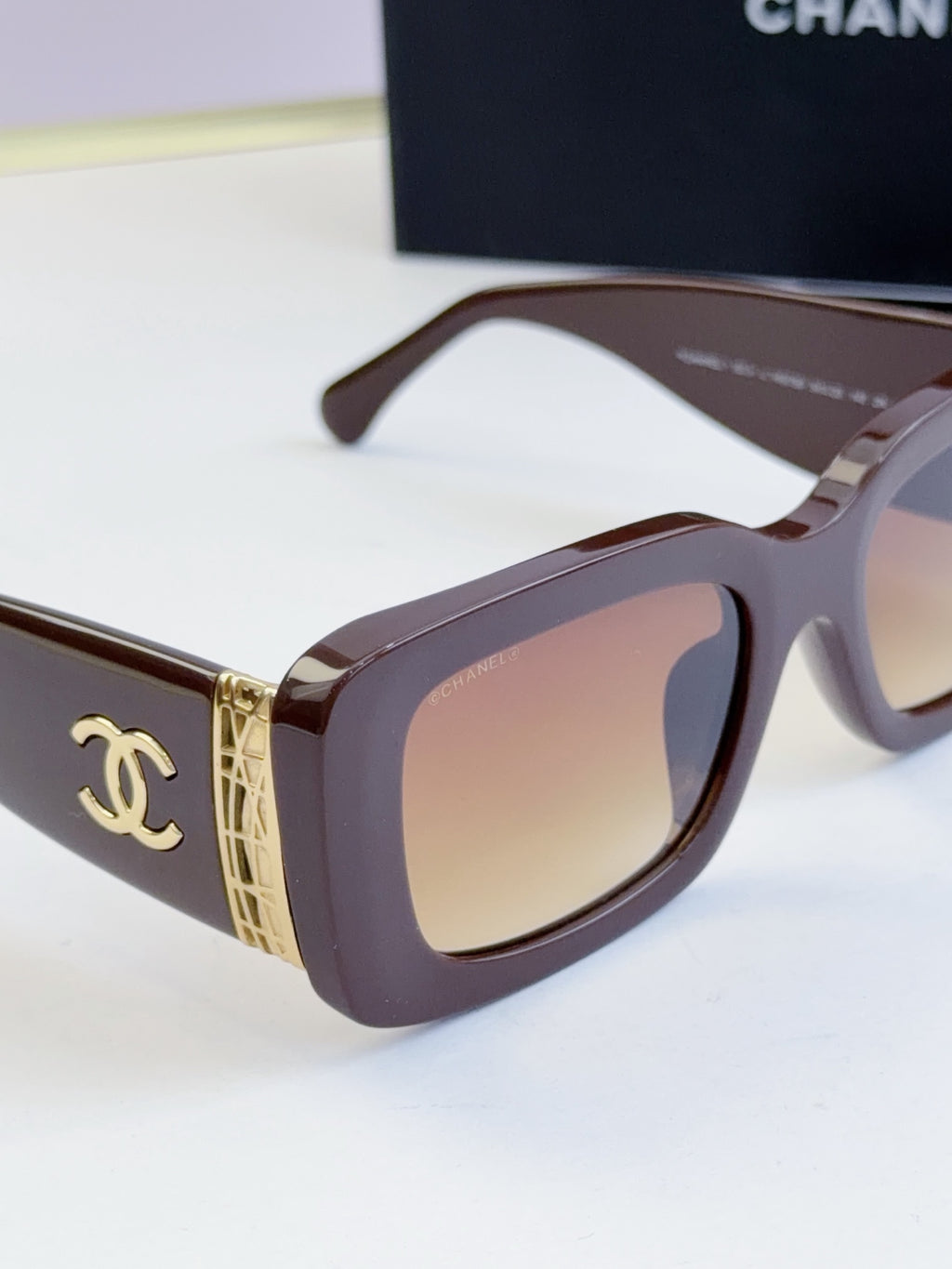 Close-up sunglasses with dark brown frames, tinted lenses, gold logo side detail