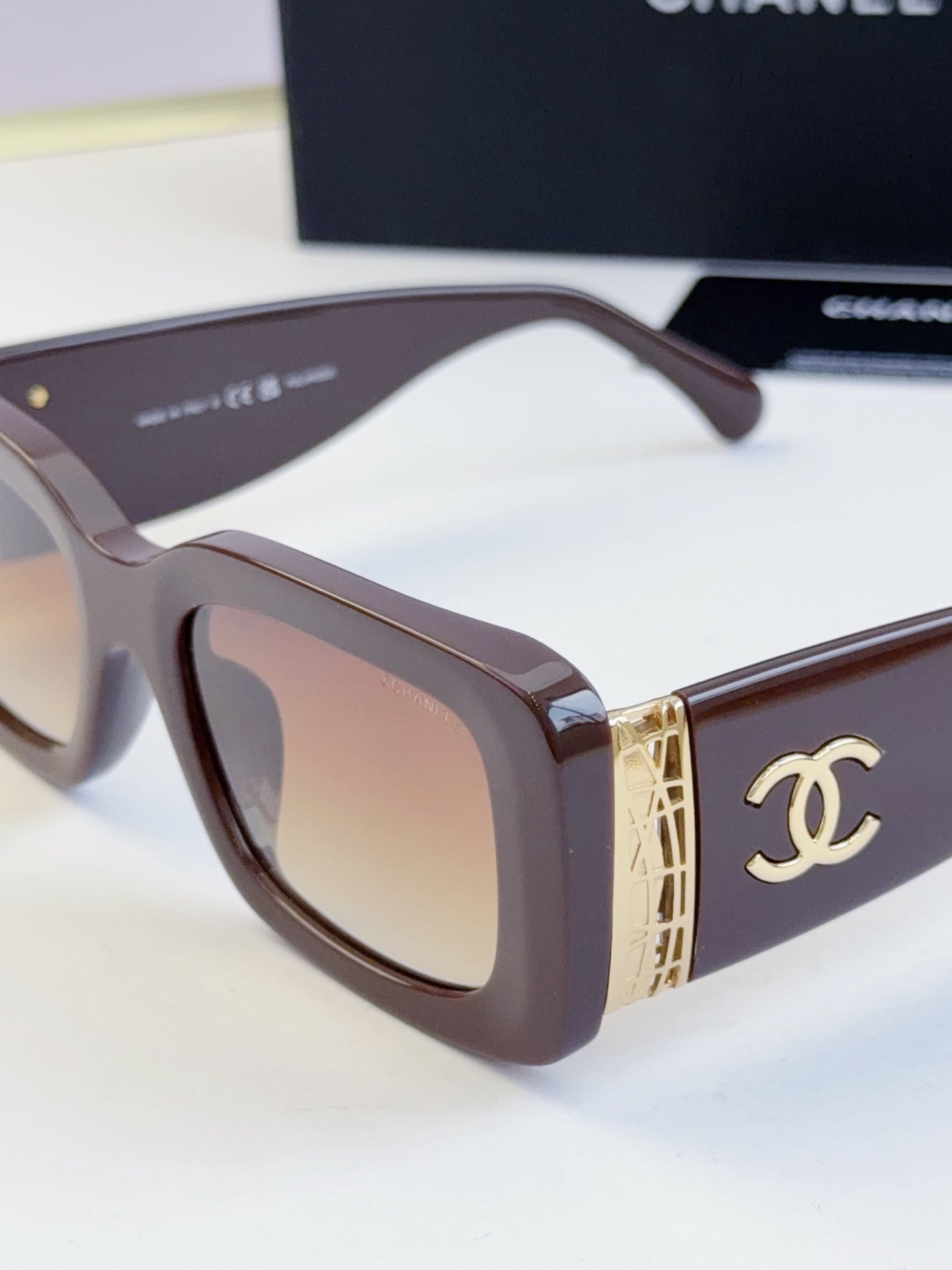 Close-up sunglasses with dark brown frames and tinted lenses, gold side emblem