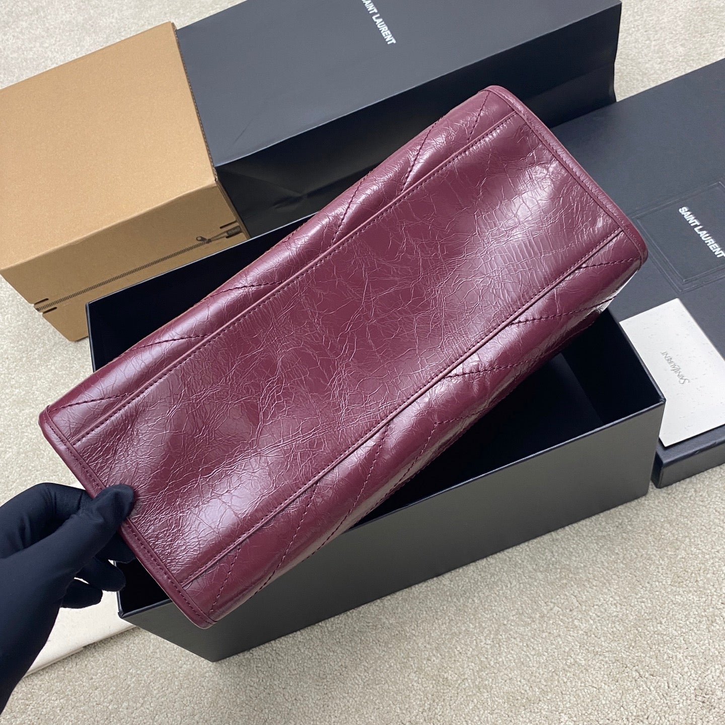 Burgundy leather tote bag with sleek front panel and gold-tone hardware, angled view