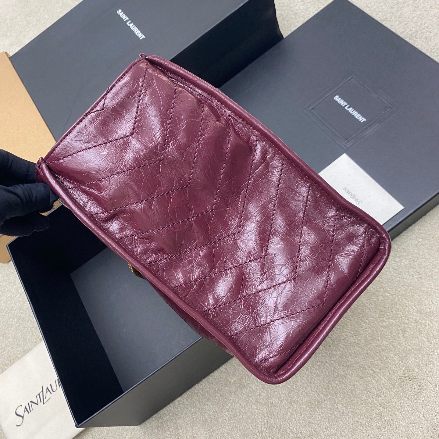 Burgundy leather tote bag with quilted diamond panels, side view and curved corners