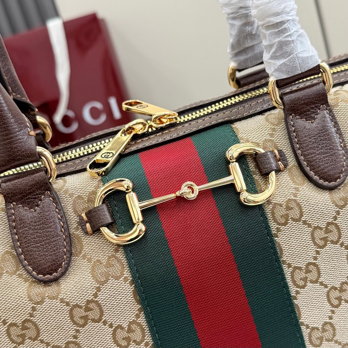 Gucci GG canvas bag close-up of gold zipper, red/green web stripe, and dark leather tabs.