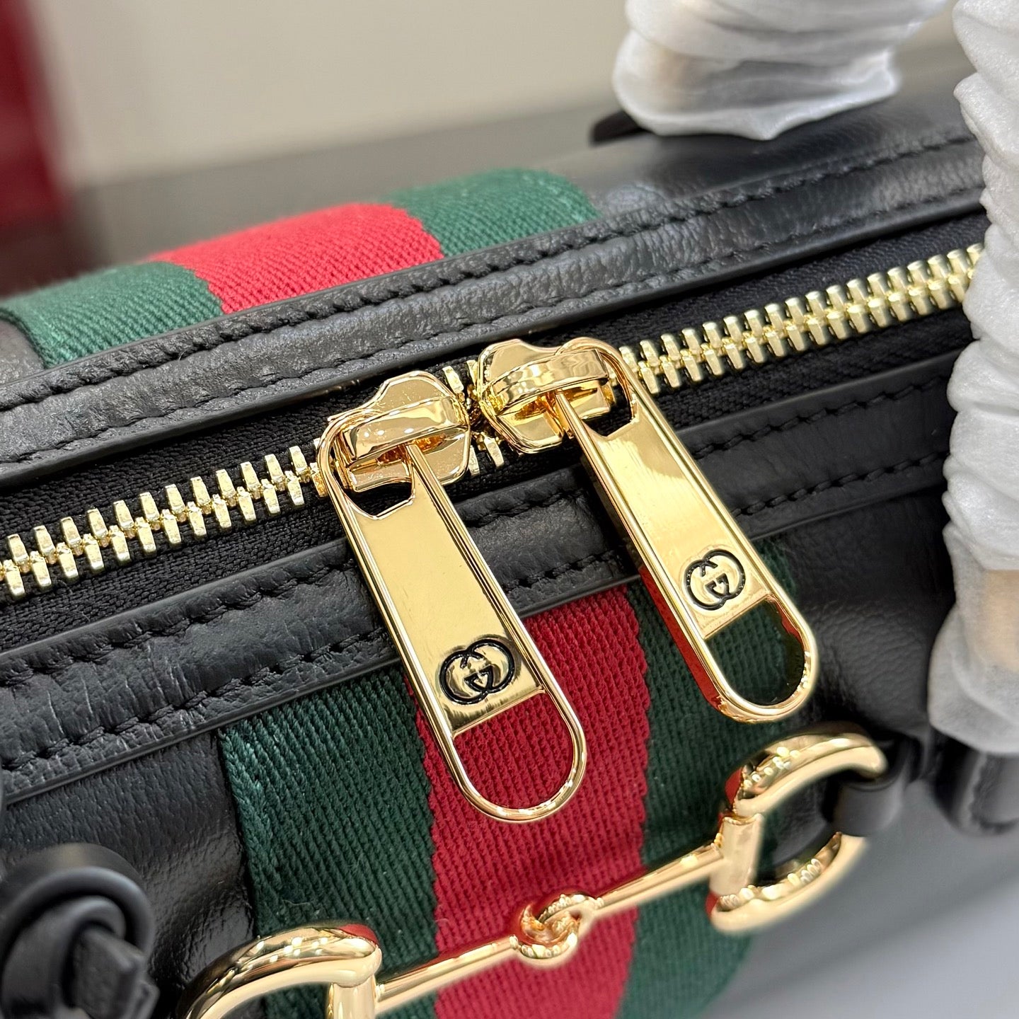 Gucci handbag zipper pull and gold-tone hardware on green-red stripe webbing.