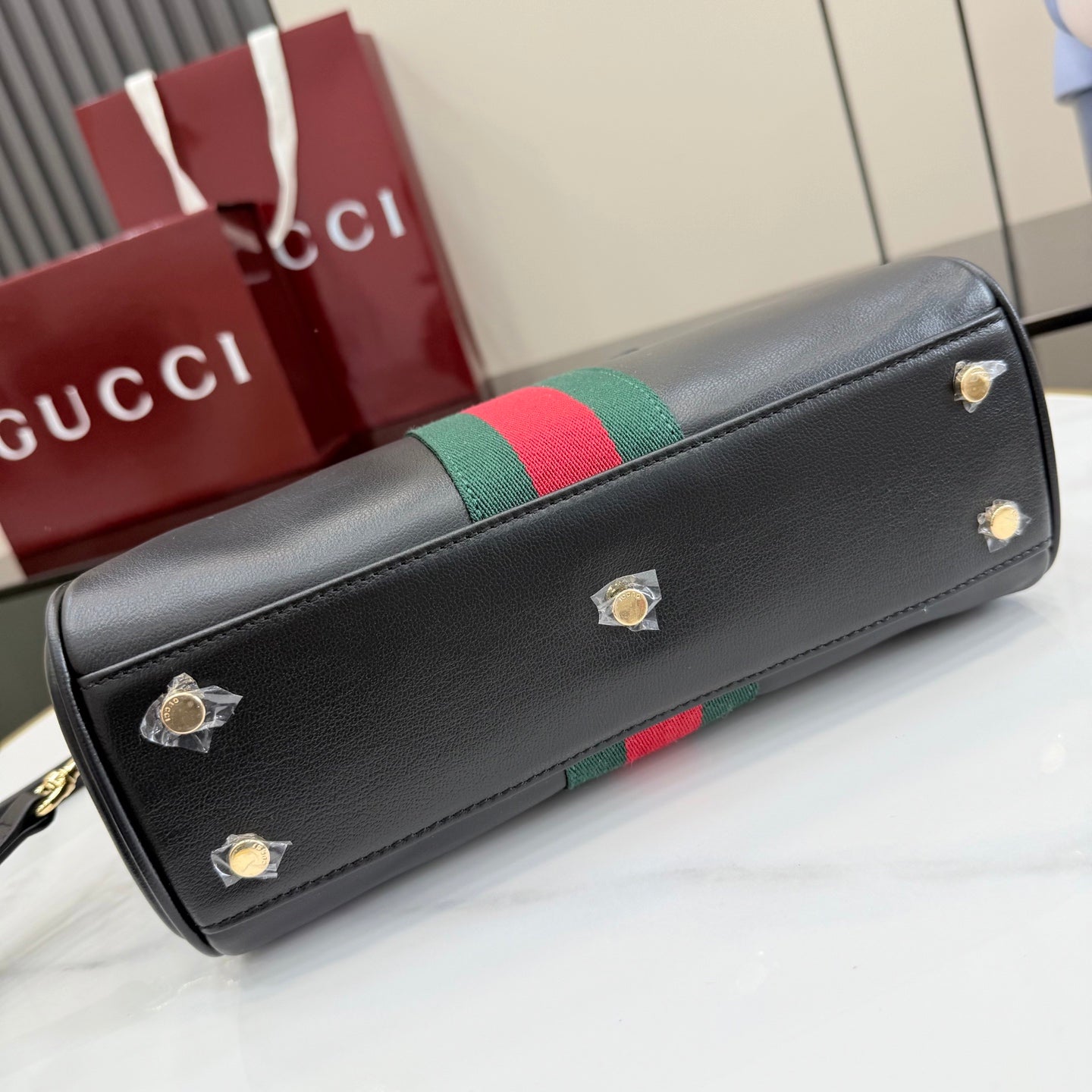 Black Gucci shoulder bag with green-red stripe trim and gold-tone stud details.