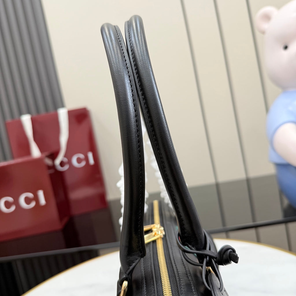 Black Gucci handbag handle detail with gold-tone zipper and leather strap.
