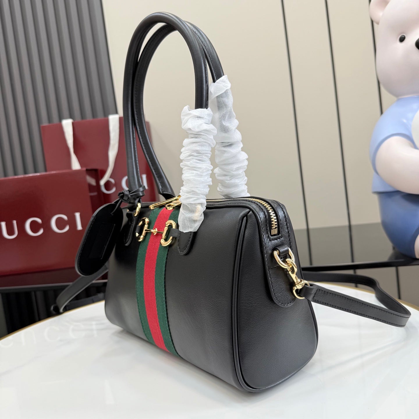 Black Gucci handbag with green-red stripe, gold-tone accents, and attached shoulder strap.