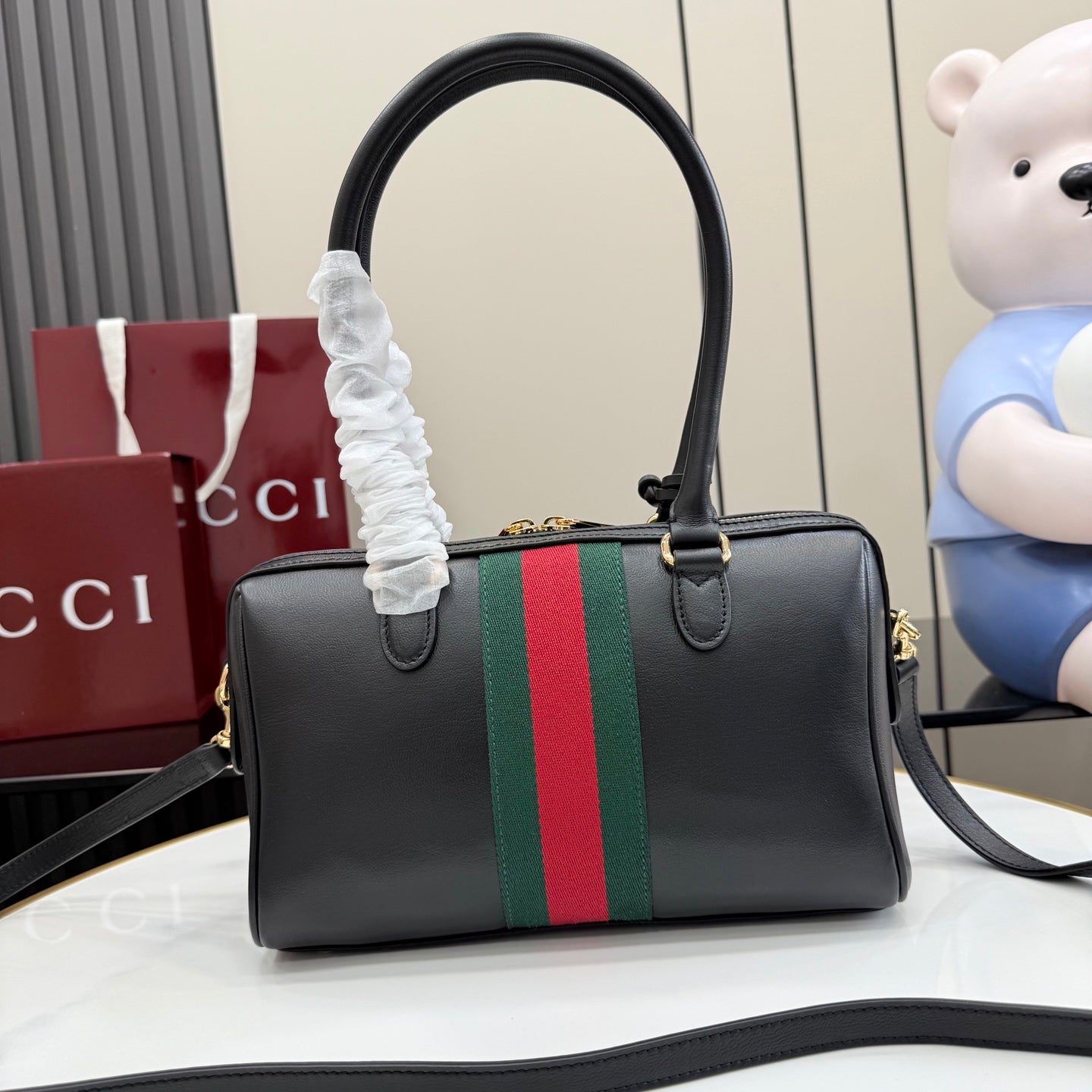 Black Gucci handbag with green-red stripe webbing and top handles; crossbody strap.