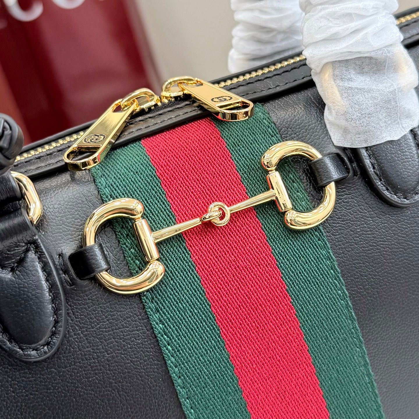 Gucci handbag close-up: green-red stripe webbing with gold-tone double hardware rings.