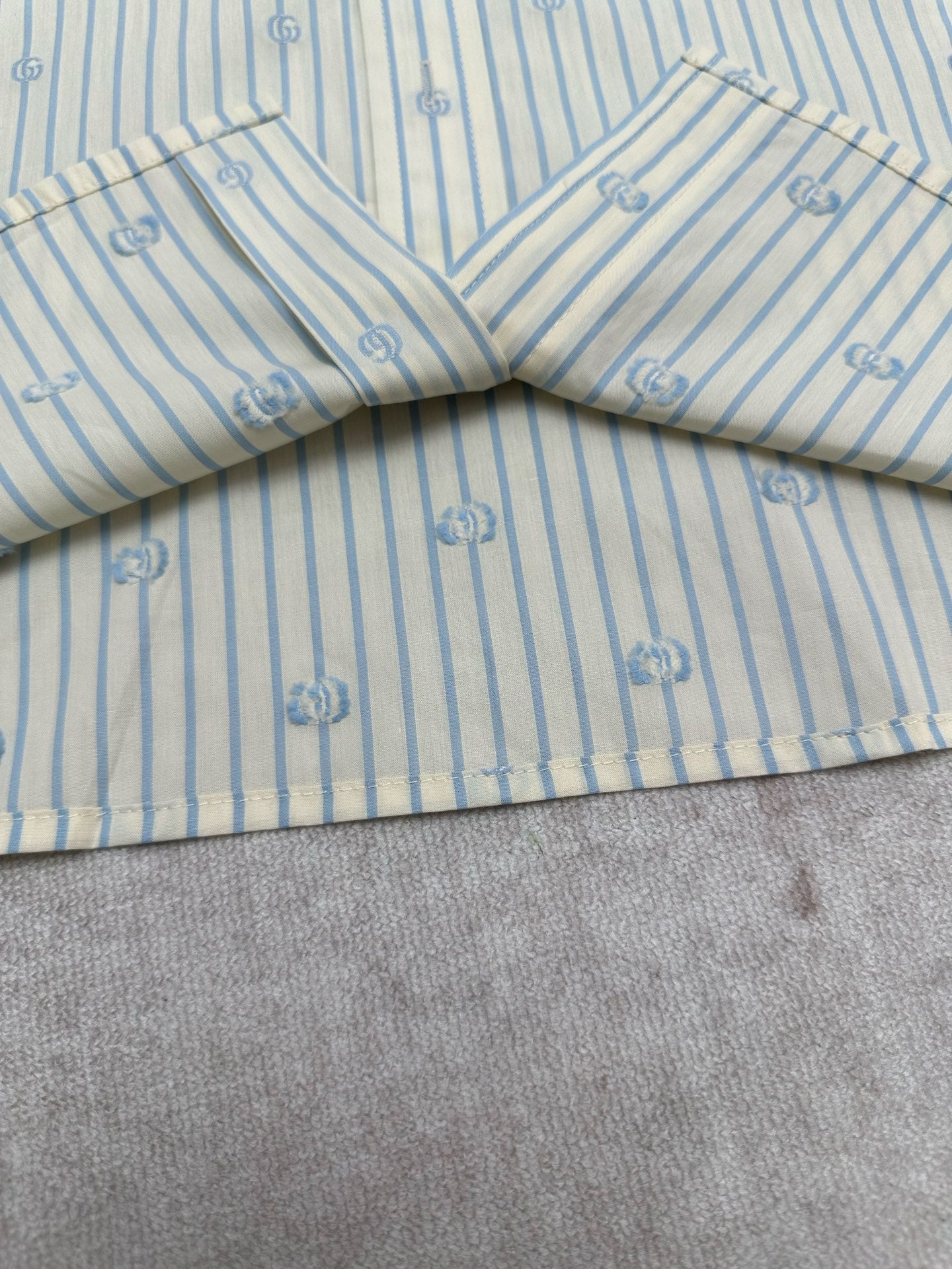 Light blue striped shirt with V-shaped yoke seam and small emblem print