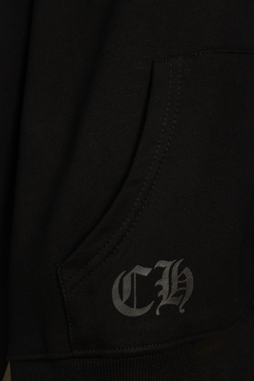 Black hoodie pocket corner with small gray embroidered monogram