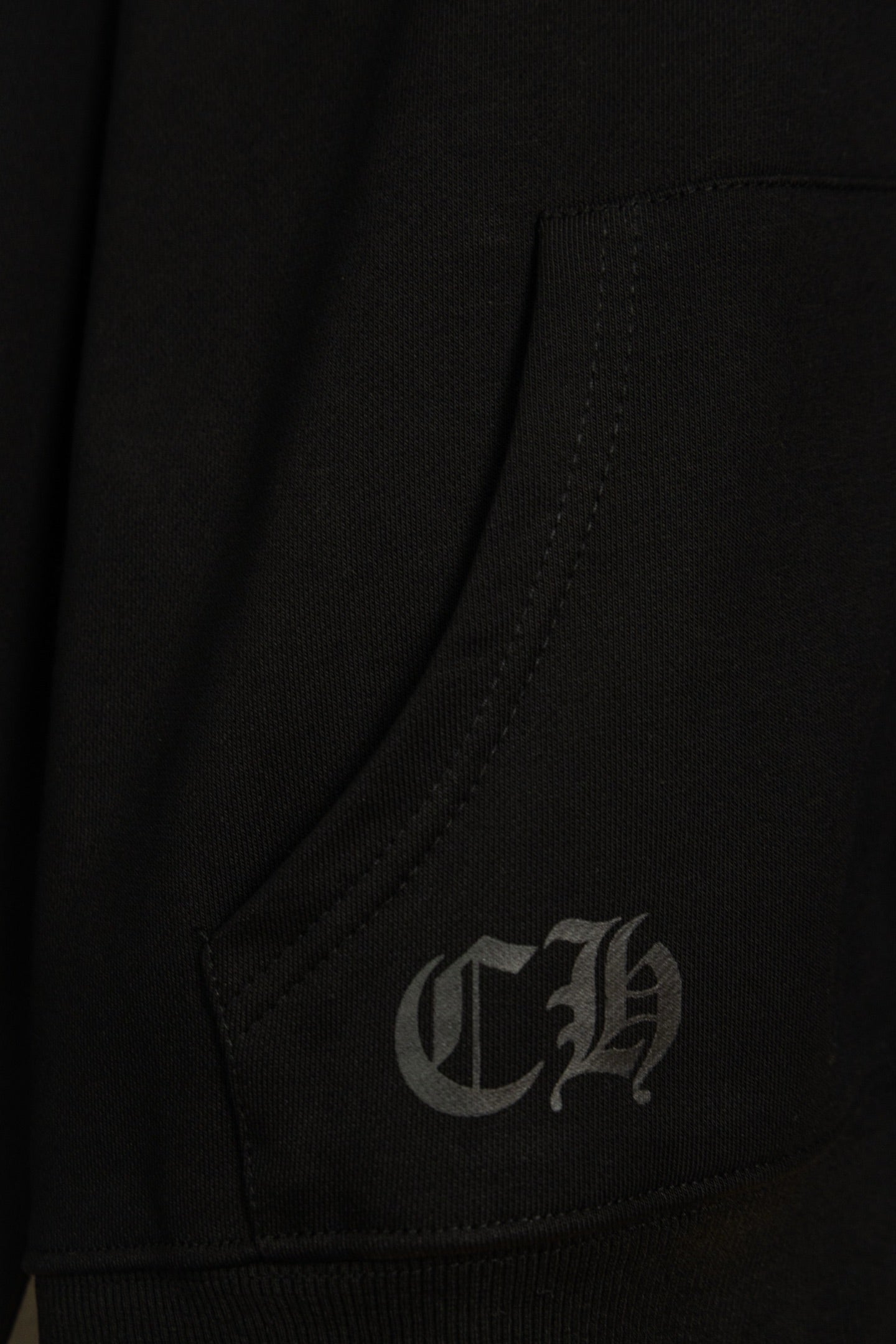 Black hoodie pocket corner with small gray embroidered monogram