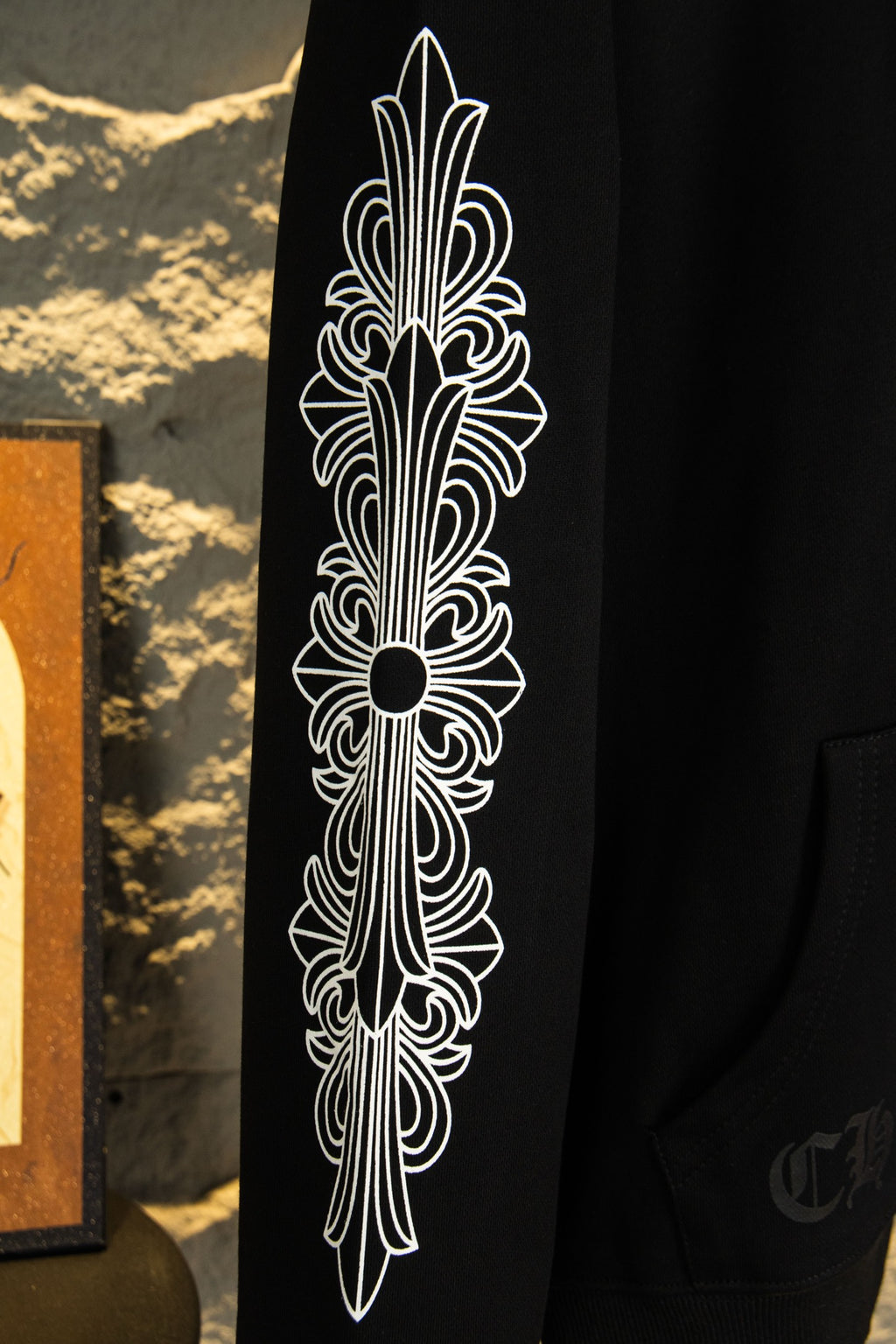 Black hoodie sleeve with tall white ornate feather-style graphic