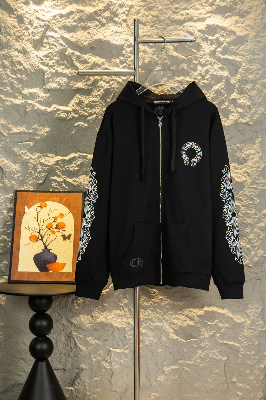 Black zip-up hoodie with hood, drawstrings, chest logo and ornate sleeve graphics