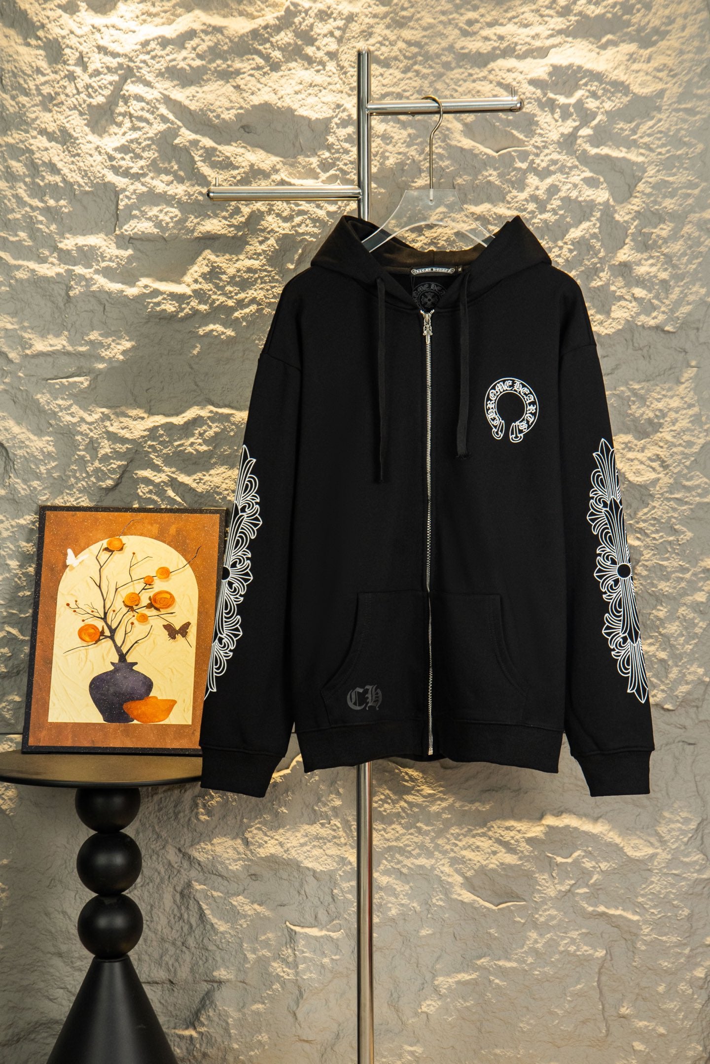 Black zip-up hoodie with hood, drawstrings, chest logo and ornate sleeve graphics