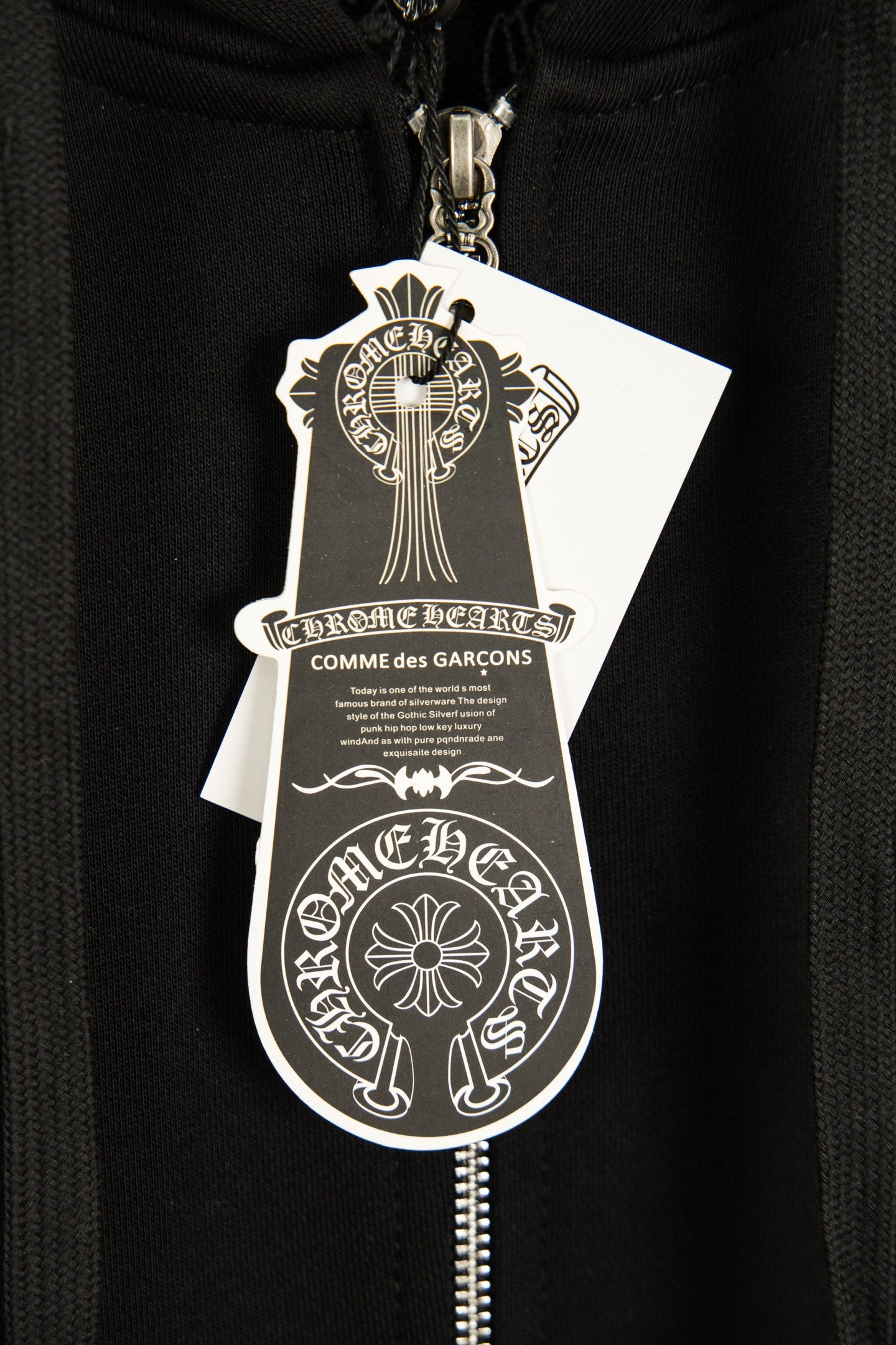 Black hoodie with silver zipper pull and hanging brand shield tag.