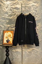 Black zip-up hoodie with hood, drawstring, and front zipper; small chest logo patch.