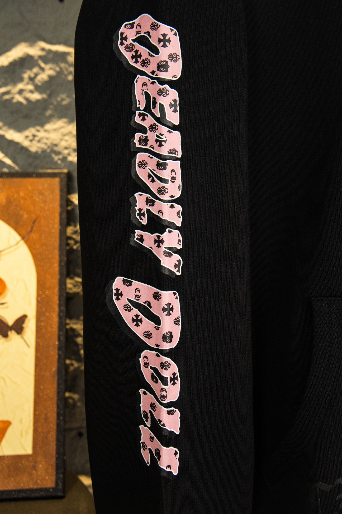 Black hoodie sleeve with pink-and-black repeating graphic text design.