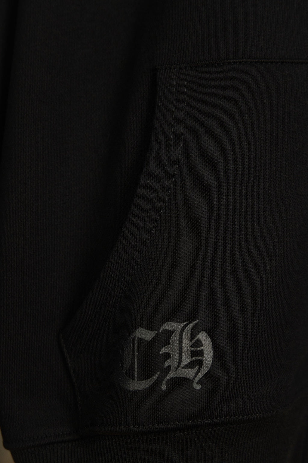 Black hoodie inner seam with stitched label; small signature graphic.